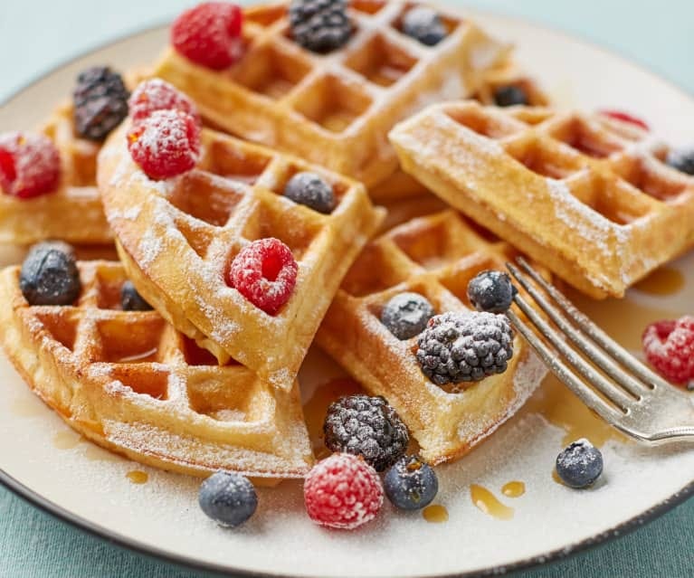 Waffles on a white plate topped with berries, syrup and powered sugar