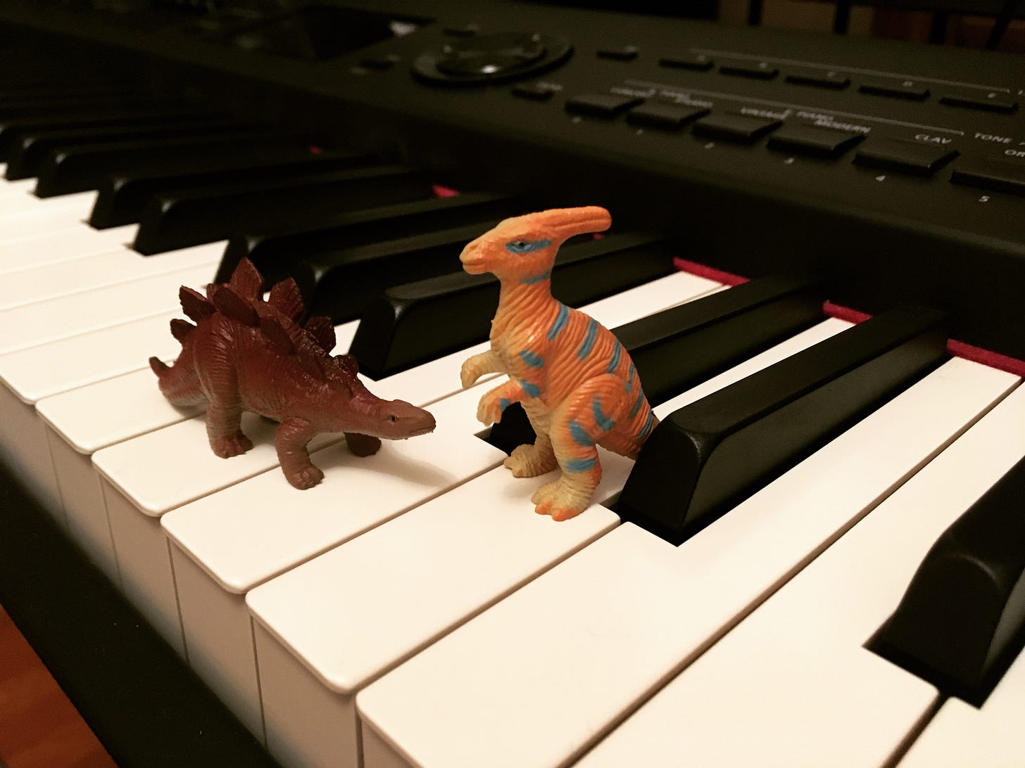 A toy stegosaurus and parasaurolophus standing next to one another on top of a piano keyboard.
