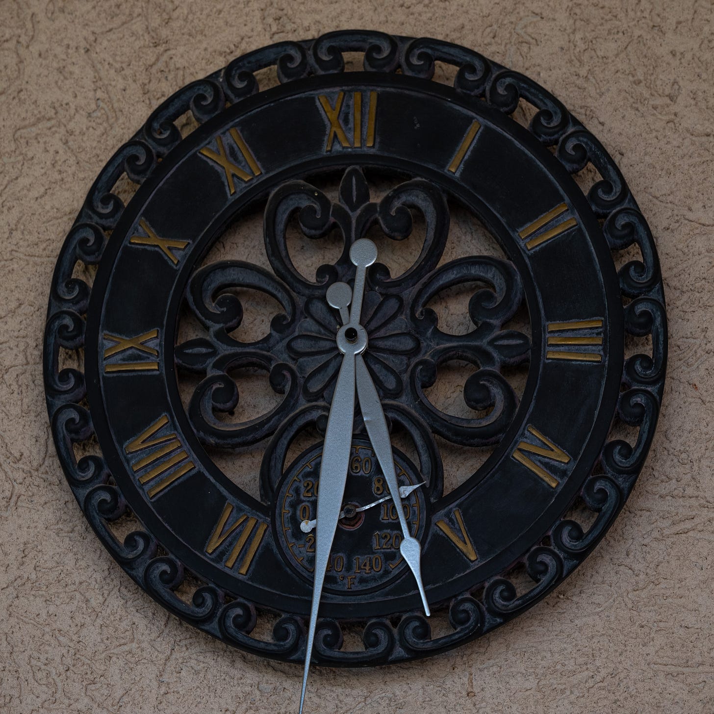 A brown cast metal clock with Roman numerals and extra large silver hands hung on a beige stucco wall