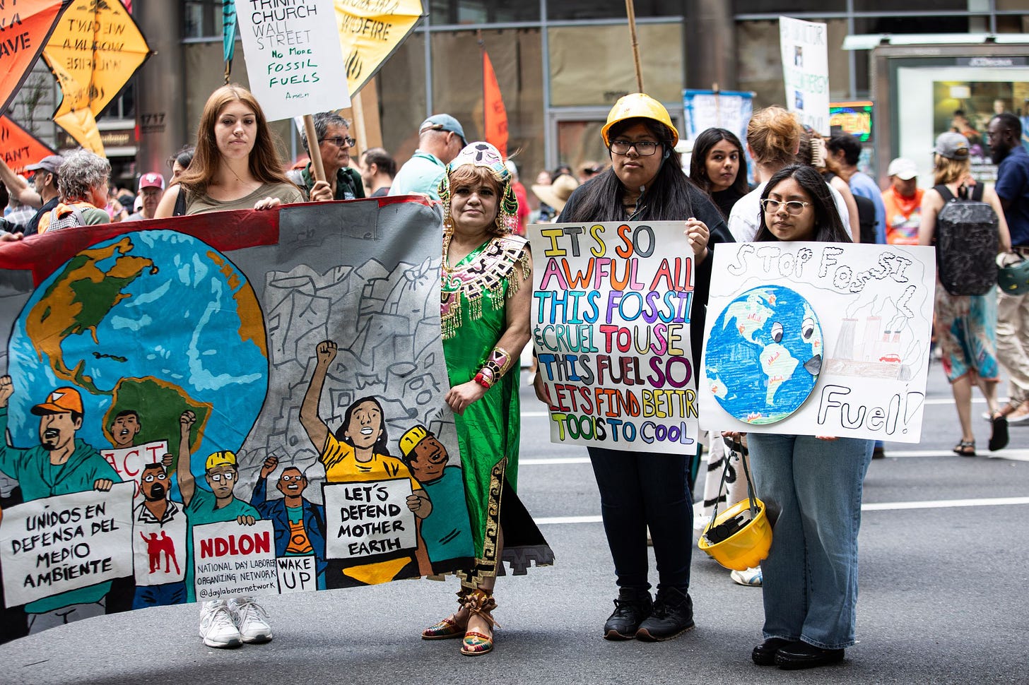 A group of people stand carrying art and signs calling for an end to fossil fuels.