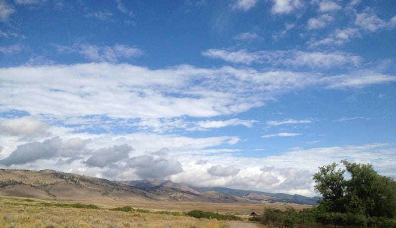 Sky and clouds over a far horizon of brown hills. The clouds near the ridgeline are small puffs moving quickly; higher clouds are hazy and long.