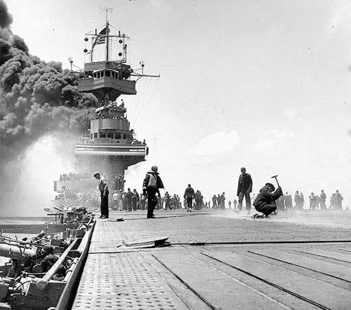 The deck of USS Yorktown is pictured.  She's just been hit by the Japanese and smoke is belching from part of the ship.