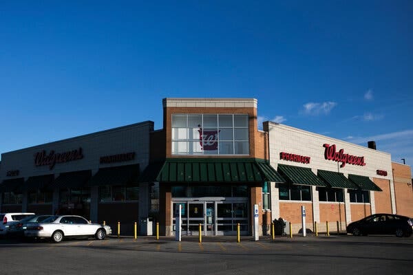 An exterior view of a Walgreens store on a bright morning. A few cars are parked in spots just outside the store.
