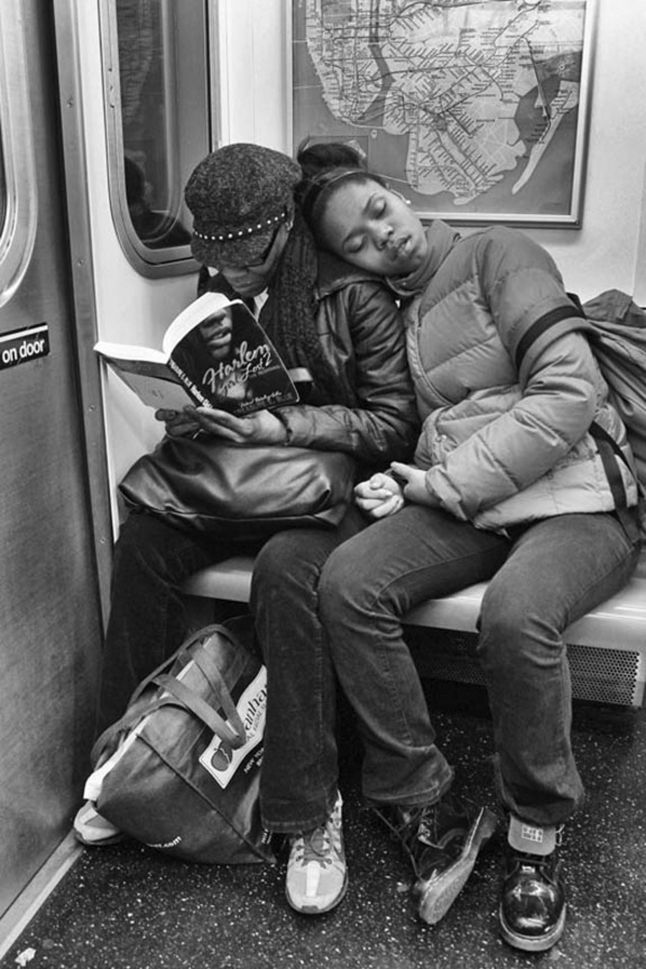 A woman reading on the #2 train while her daughter slumbers beside her.