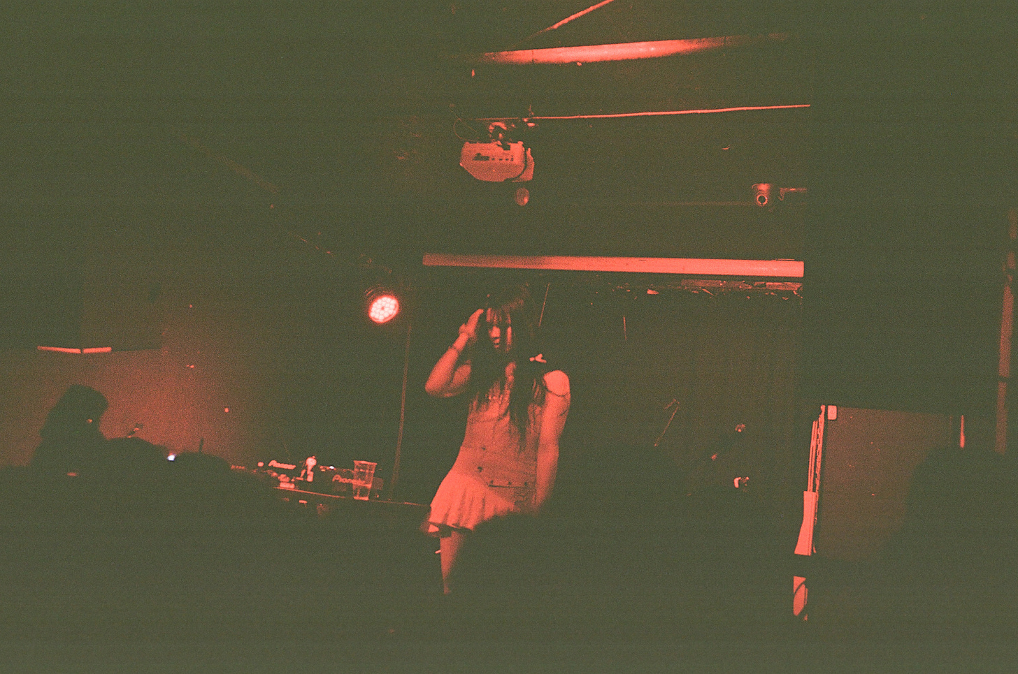 In a 35mm film photo, red light illuminates an otherwise black scene, in which Princess Xixi stands onstage, running a hand through her hair