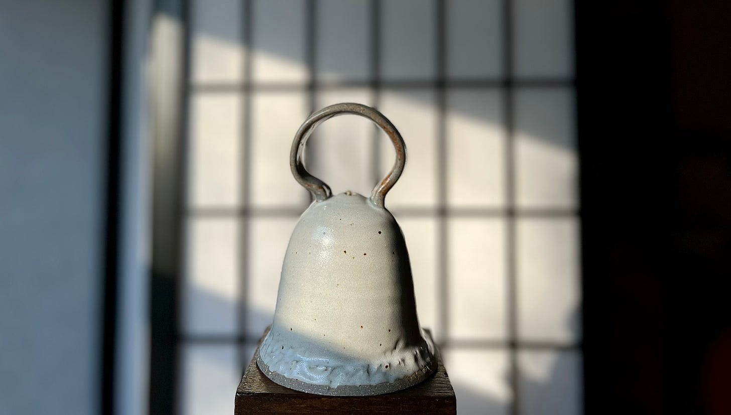 off-white ceramic bell with curved gray handle on top