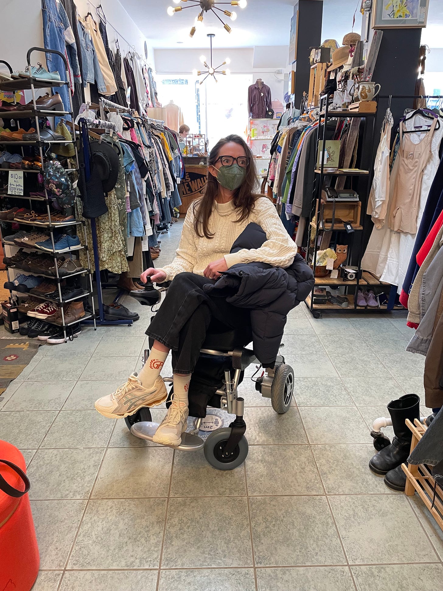 a white woman in a wheelchair and a mask looks around a vintage shop