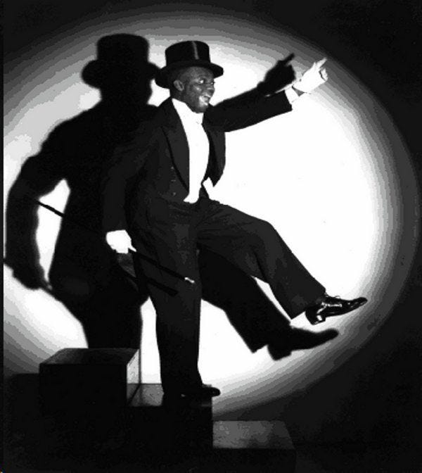 This may contain: a black and white photo of a man in a top hat with his shadow on the wall