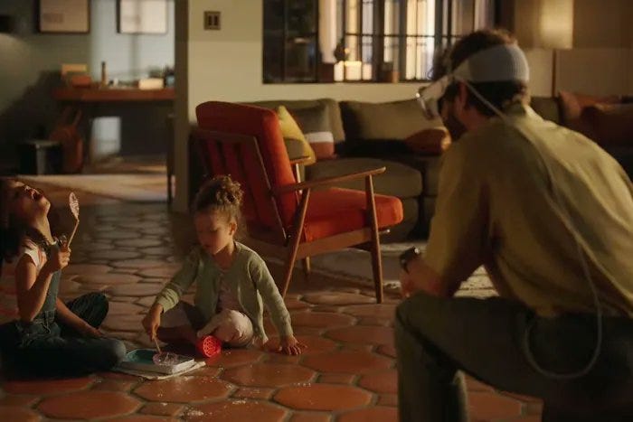 Two girls sit on the floor playing with bubbles; a dad is watching them but he's wearing the Vision Pro.