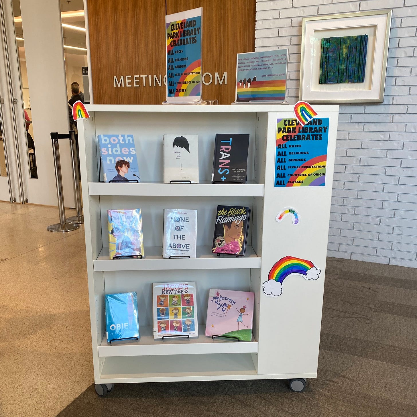A sign on the bookshelf says Cleveland Park Library celebrates all races, religions, genders, sexual orientations, countries of origin, and classes. Three additional pride rainbows are also on the bookshelf.
