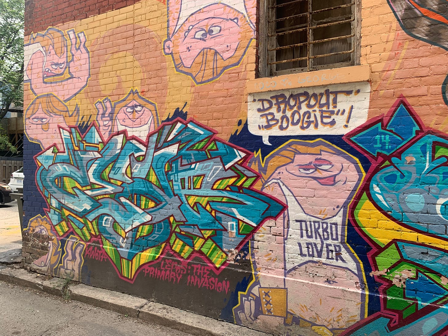 Graffiti art with blue lettering with pink outlines and the signature "KWOTA," ith cartoon characters of white men in tank tops, one of which says "TURBO LOVER" on the front.