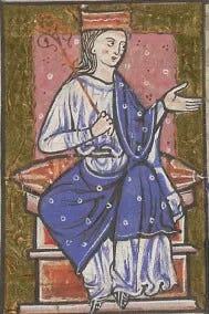 The lady Æthelflæd sits on what looks like a throne holding a rod in her hand. She's dressed in a light blue robe covered in a dark blue mantle studded with dots