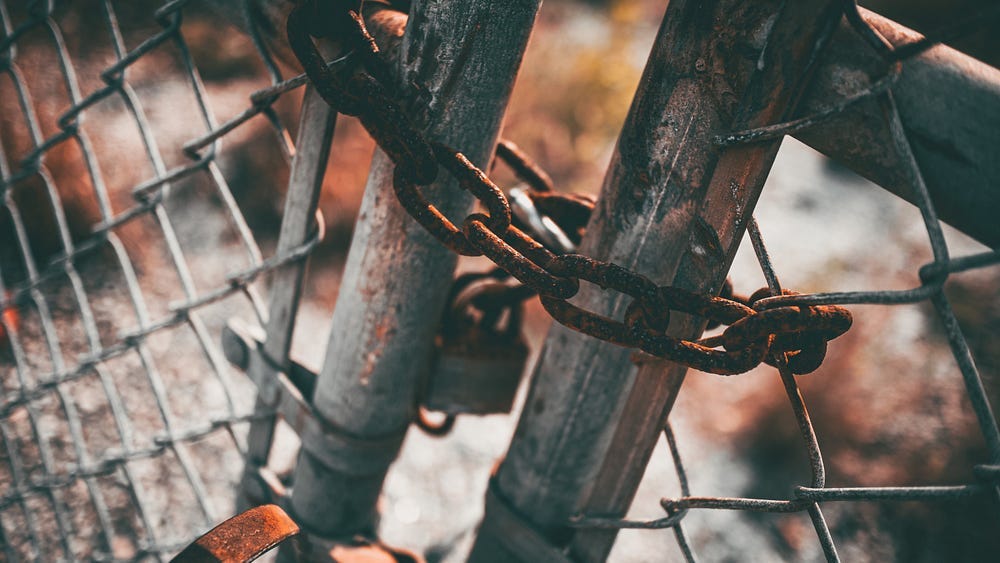 Rusted chains and a padlock holding a gate tightly shut. Rusted chains and a padlock holding a gate tightly shut.