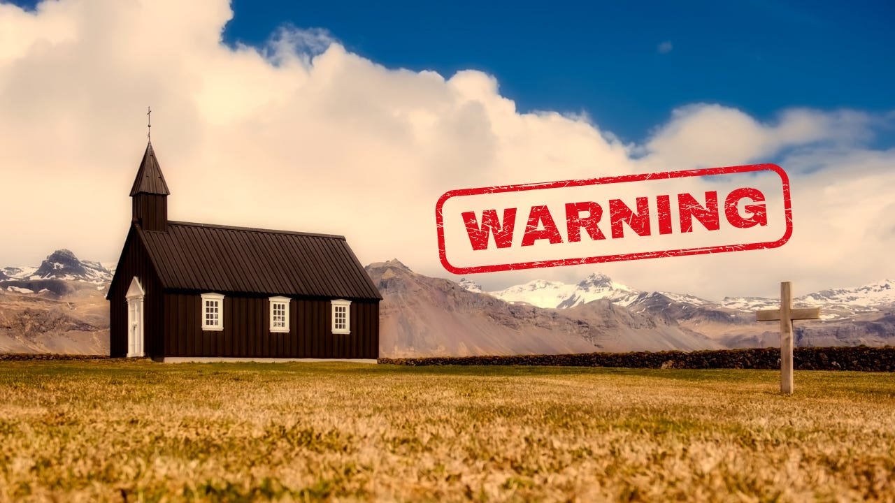 A church building in a meadow in front of mountains next to the word "Warning."