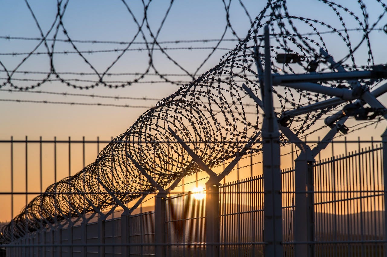 coils of razor wire sit atop metal fencing with the sun setting in the background coils of razor wire sit atop metal fencing with the sun setting in the background
