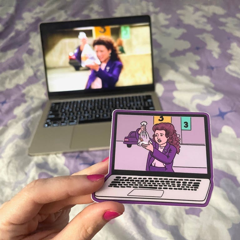 Sio holding up the sticker of her illustration of Elaine holding up a fish in the parking garage in front of a laptop showing the very same clip from its Seinfeld episode