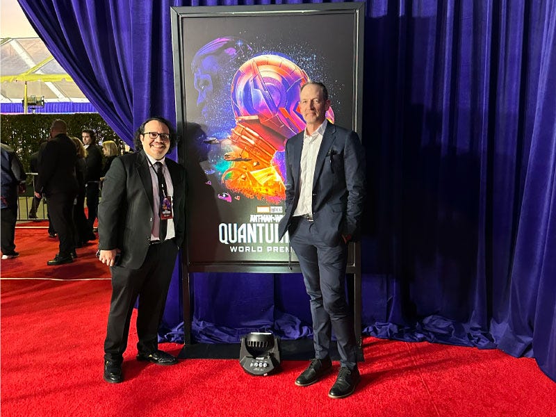 Henry Barajas and Terry Dotson in suits taking a picture at the Marvel Studios' Ant-Man and The Wasp: Quantumania red carpet premiere