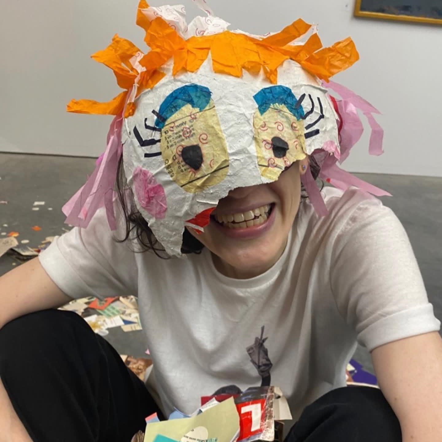 A white woman sits with a huge grin, most of her face obscured by the remains of a pinata worn as a hat
