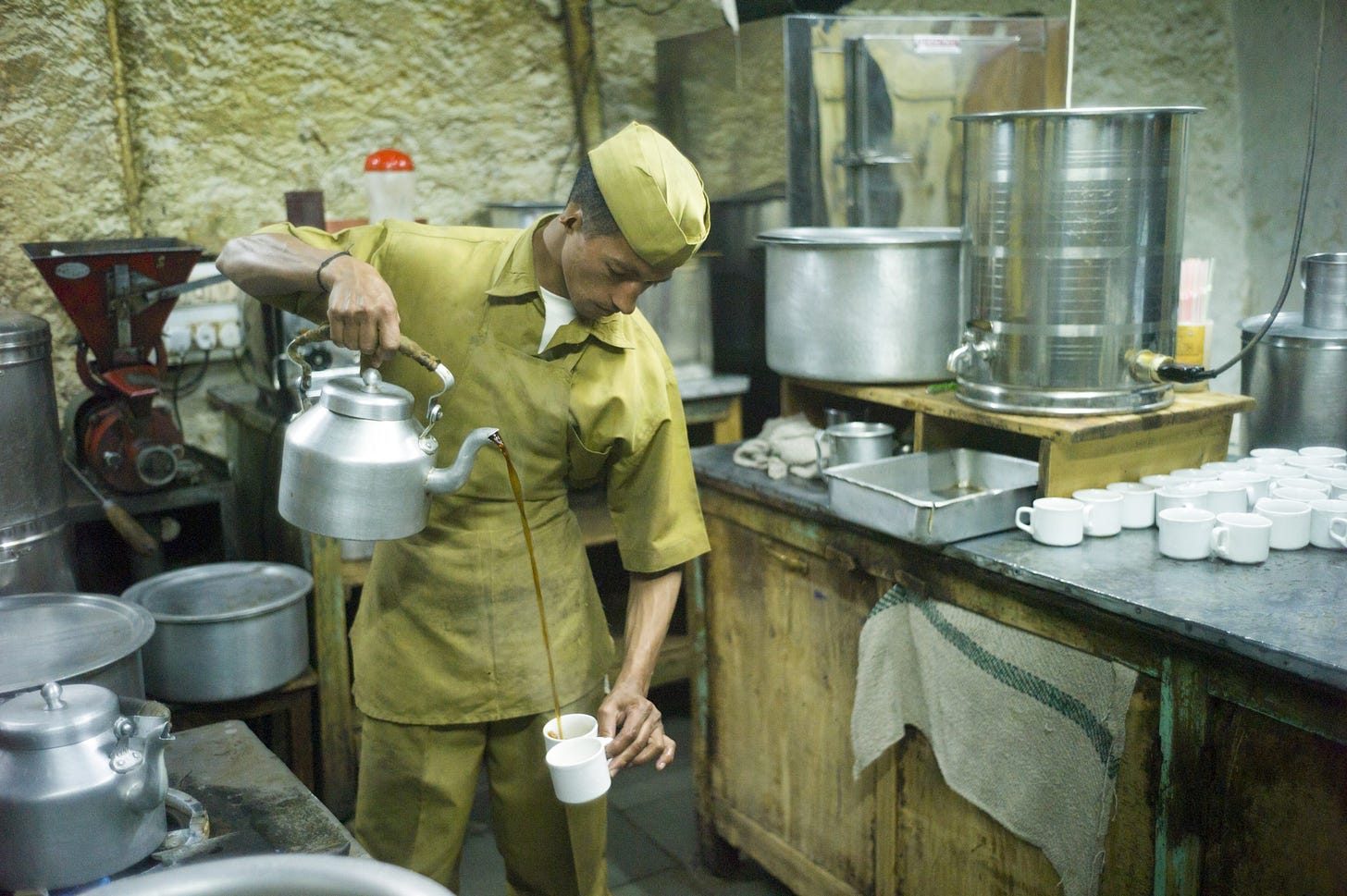 A worker pours coffee from a kettle into two cups in the kitchen of an Indian Coffee House location
