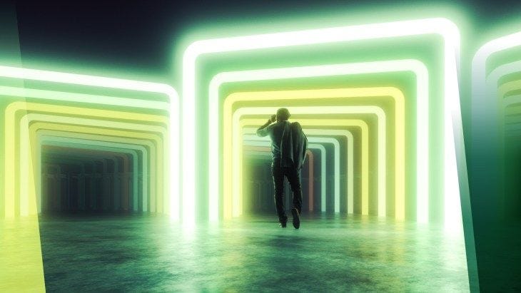 Foto de homem de costas com jaqueta sobre o ombro caminhando em chão de cimento sob corredor de portais com contorno de luzes neon predominantemente verdes e amarelas.