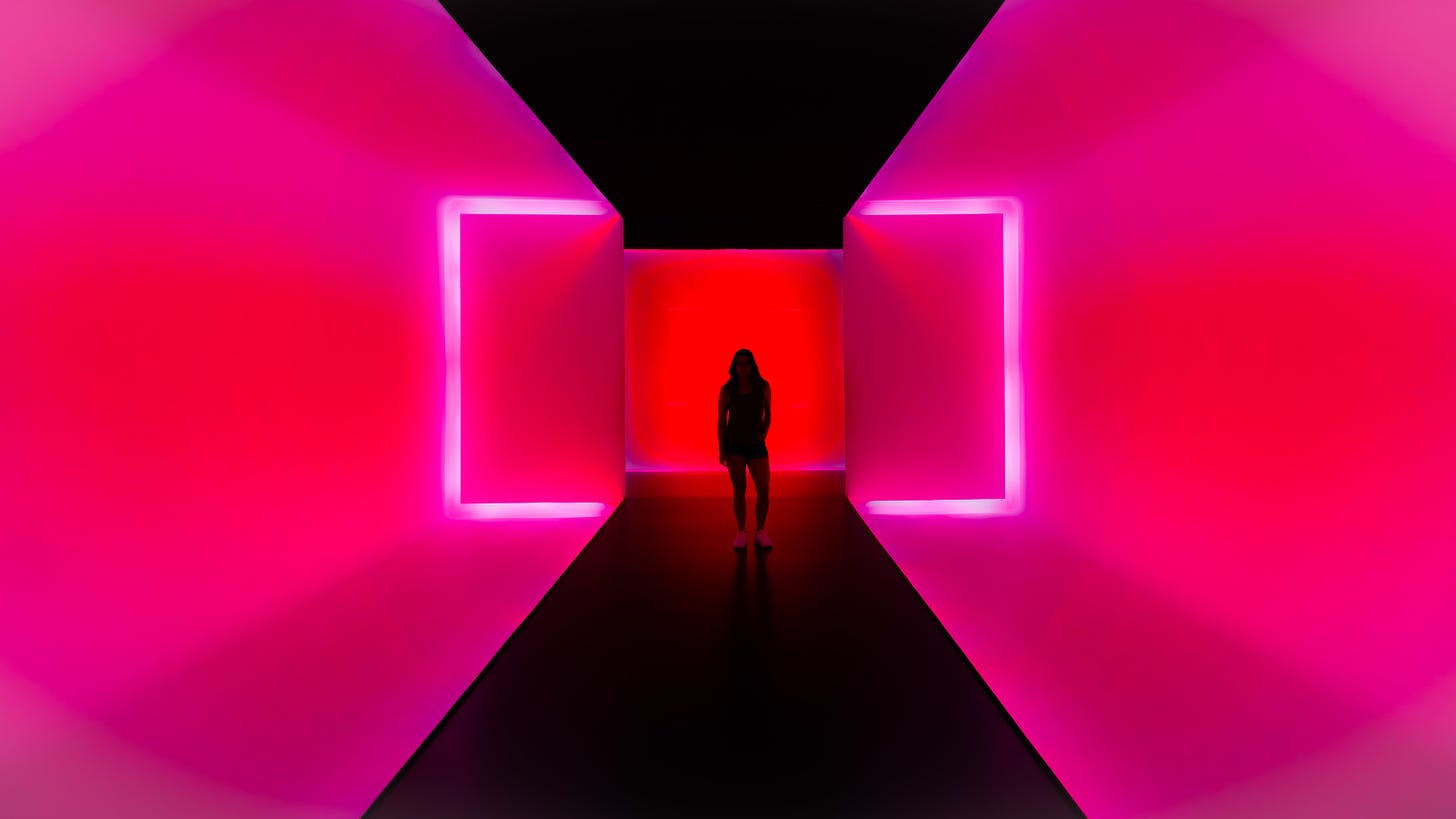 A young person stands at the end of a long, neon-pink corridor.  It is bright and dark all at once.  It is fun, '80s and very Me.