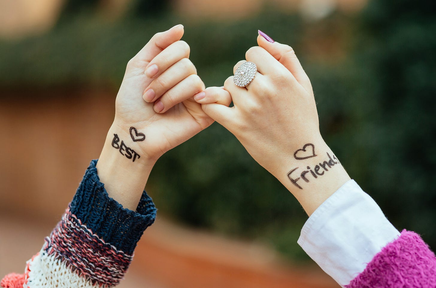 Two hands in pinky ring embrace with Best Friend written on their wrists.