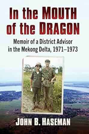 The book cover of In the Mouth of the Dragon: Memoir of a District Advisor in the Mekong Delta, 1971-1973 by John B. Haseman features a photograph of two men in military uniforms standing together in a rural landscape, with a river and fields visible in the background, framed by bold red and black title text above their image.