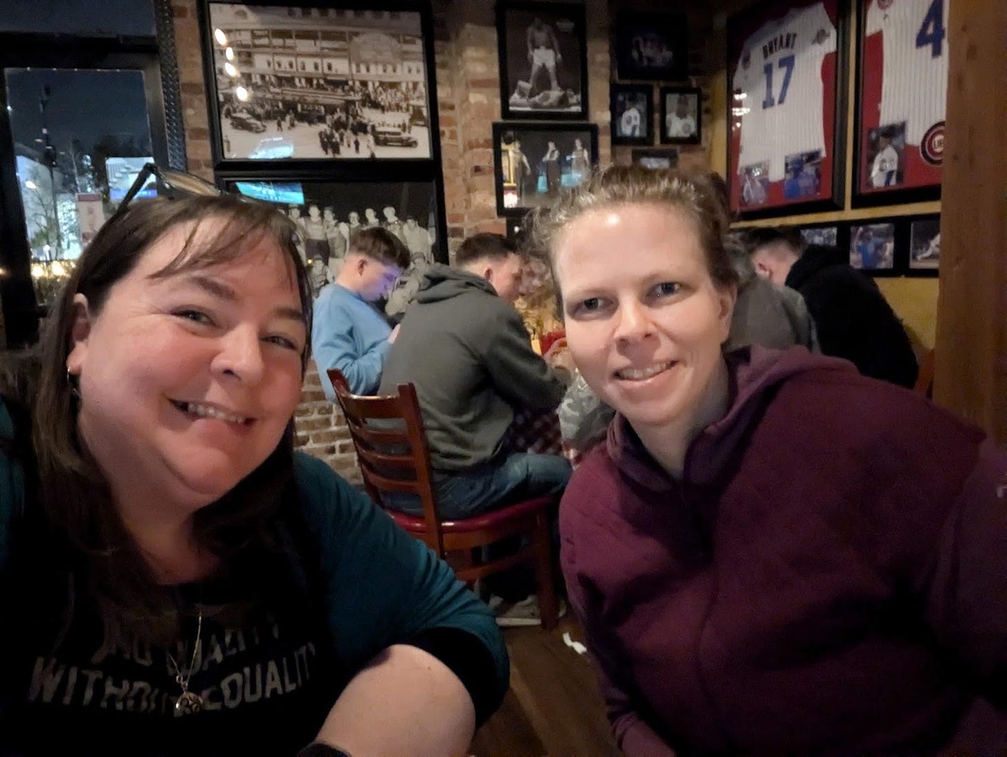 Liz taking a selfie of herself and Megan, out at a casual restaurant with old photos and sports jerseys on the wall.