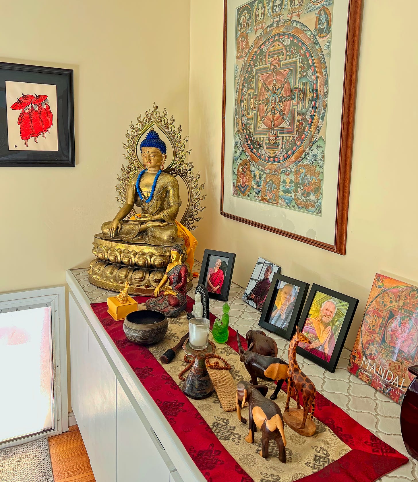 Photo of the corner of a room with a large Buddha a mandala and numerous Buddhist photos and objects