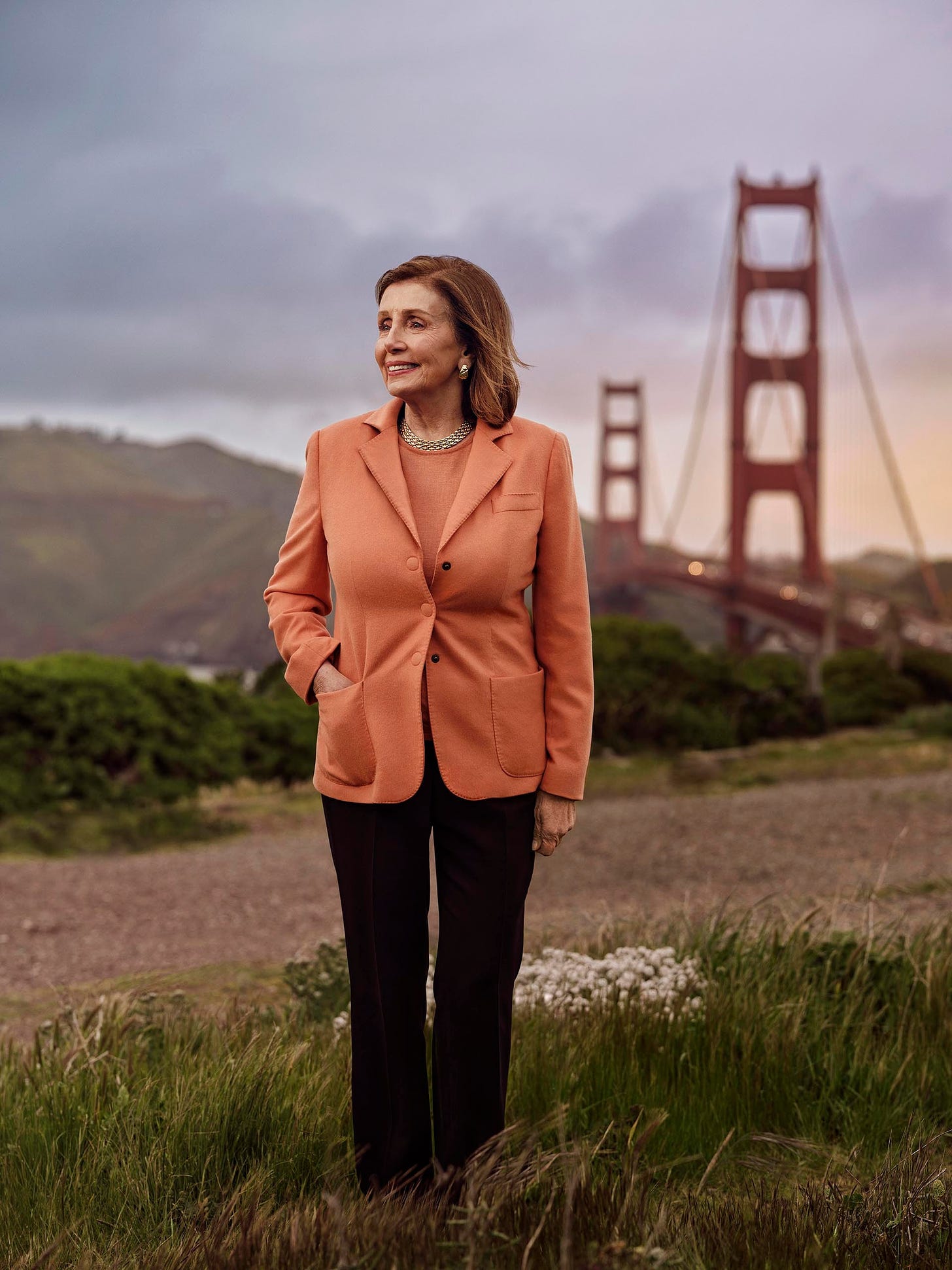 Nancy Pelosi standing with a hand in her coat pocket. The Golden Gate Bridge is visible in the background.