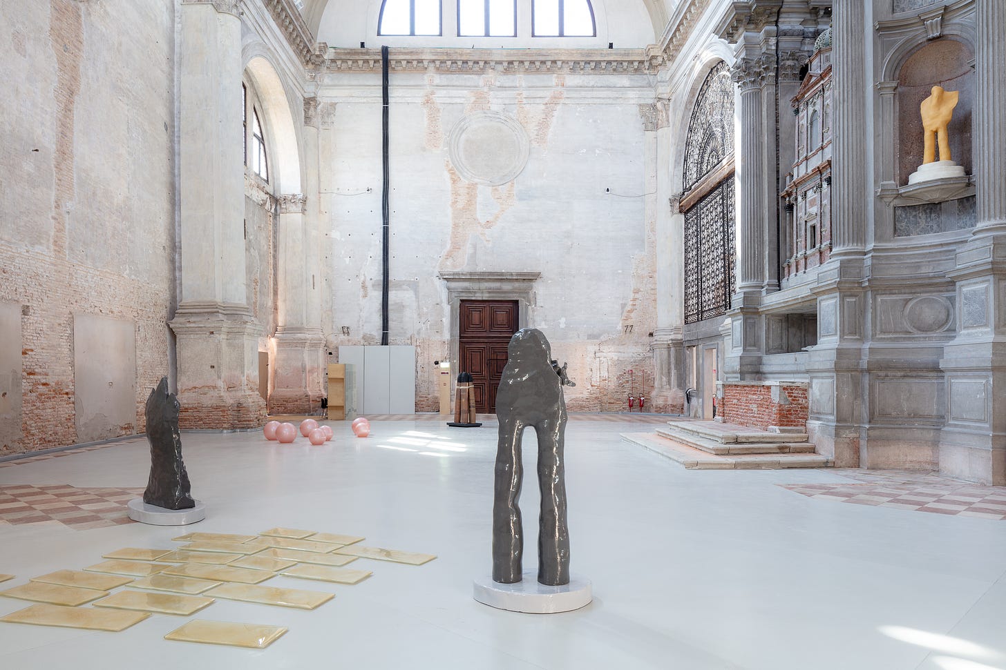 A large bright church wing is filled with sculptures and glass objects on the floor.