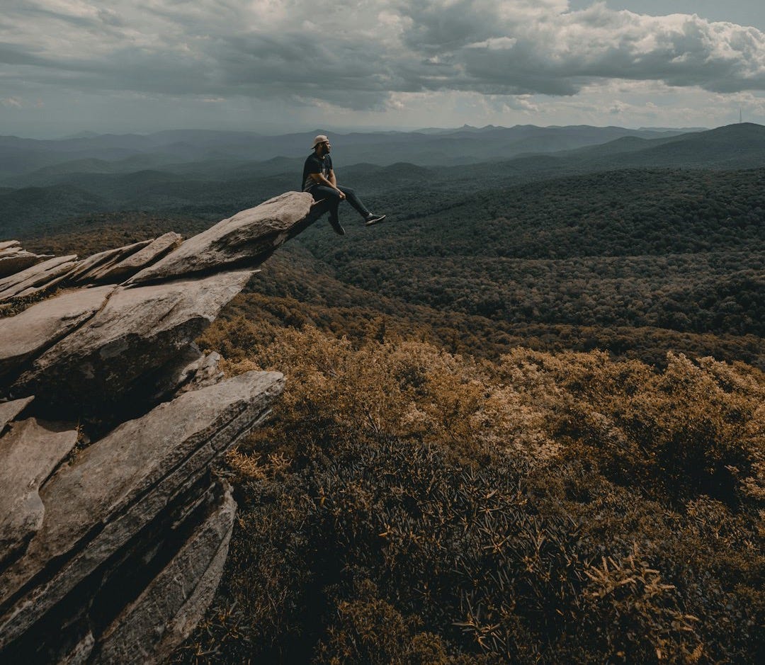 person sitting on brown cliff person sitting on brown cliff