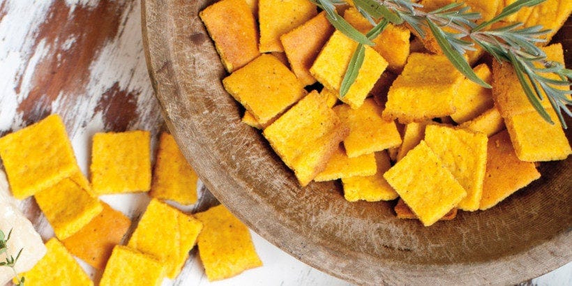 Photo of crispy sweet potato squares in a rustic bowl on a half painted wooden table with roseemary sprigs for decoration.