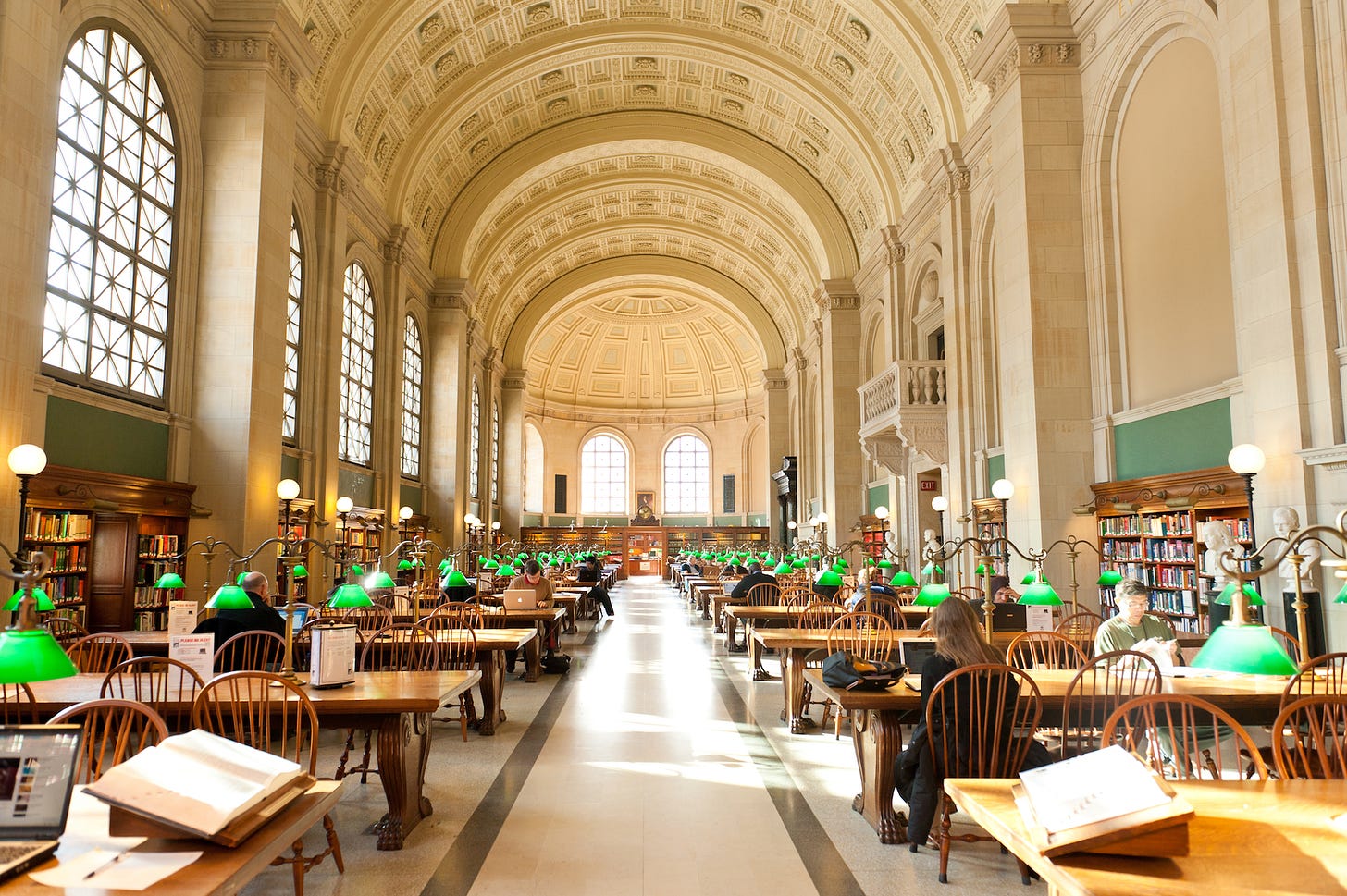 The Reading Room at the Boston Public Library: a vaulted space with rows of reading tables and green lamps
