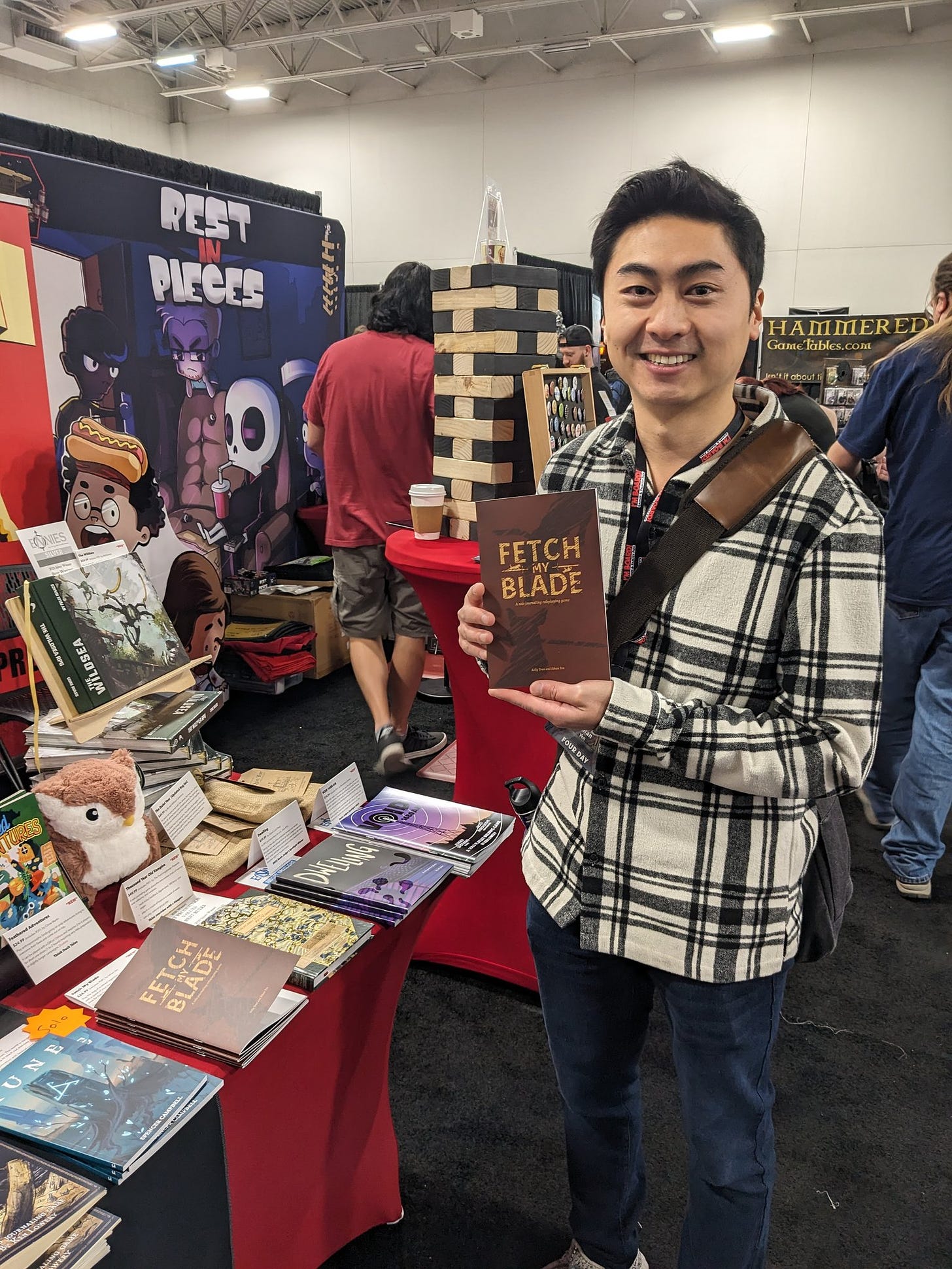 Ethan Yen standing with a copy of Fetch My Blade next to the IPR booth at Gamehole Con