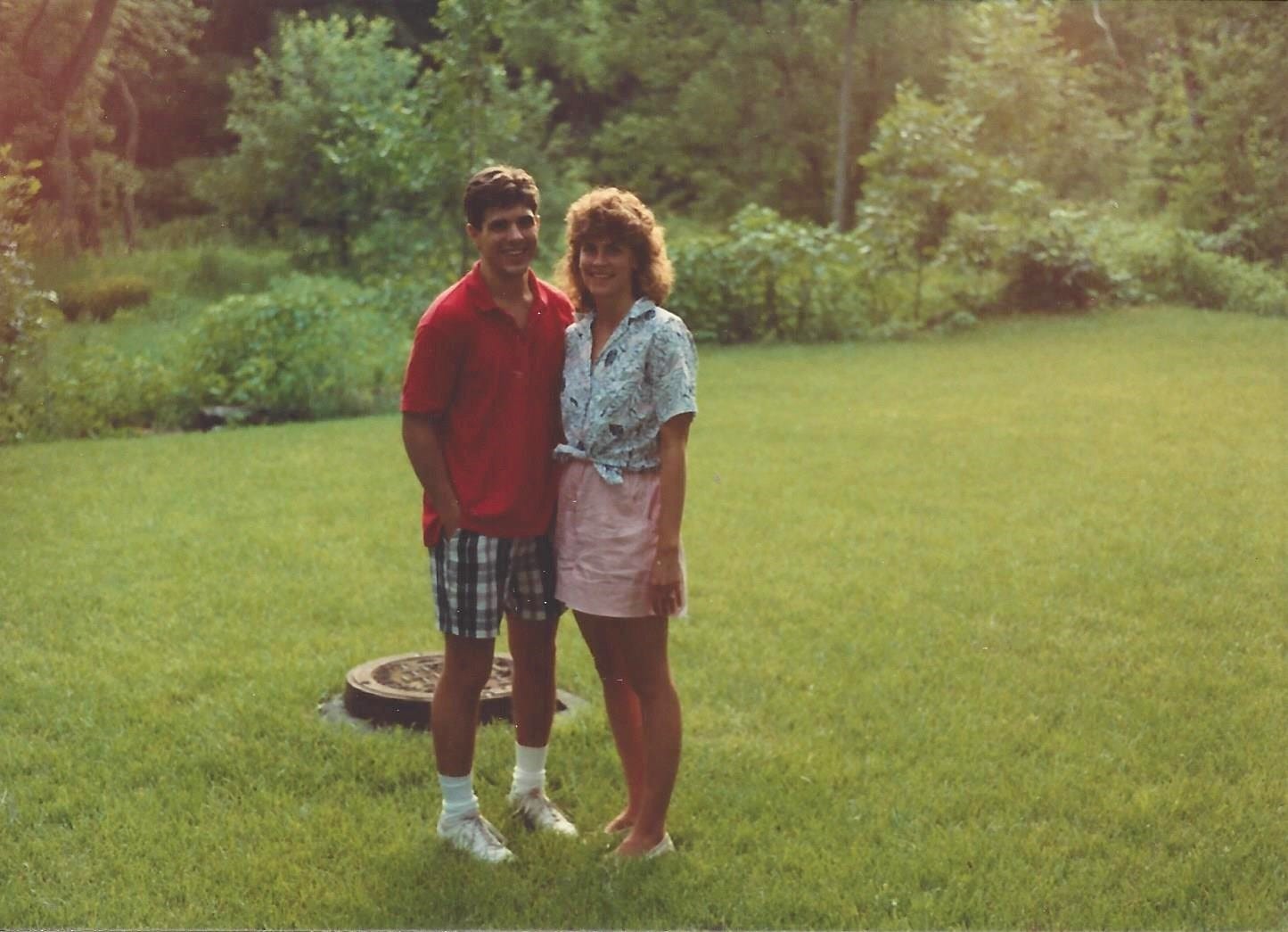 Young couple posing proudly in their backyard, against a backdrop of woodlands