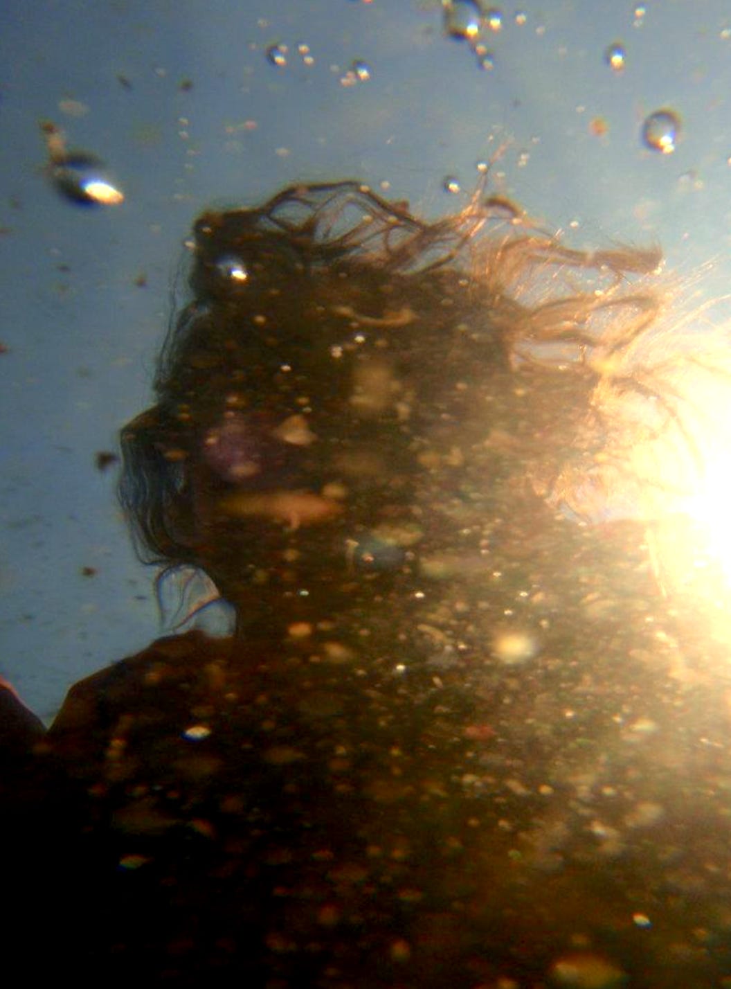 The reflection of a woman's head, hair wild, face obscured, in water