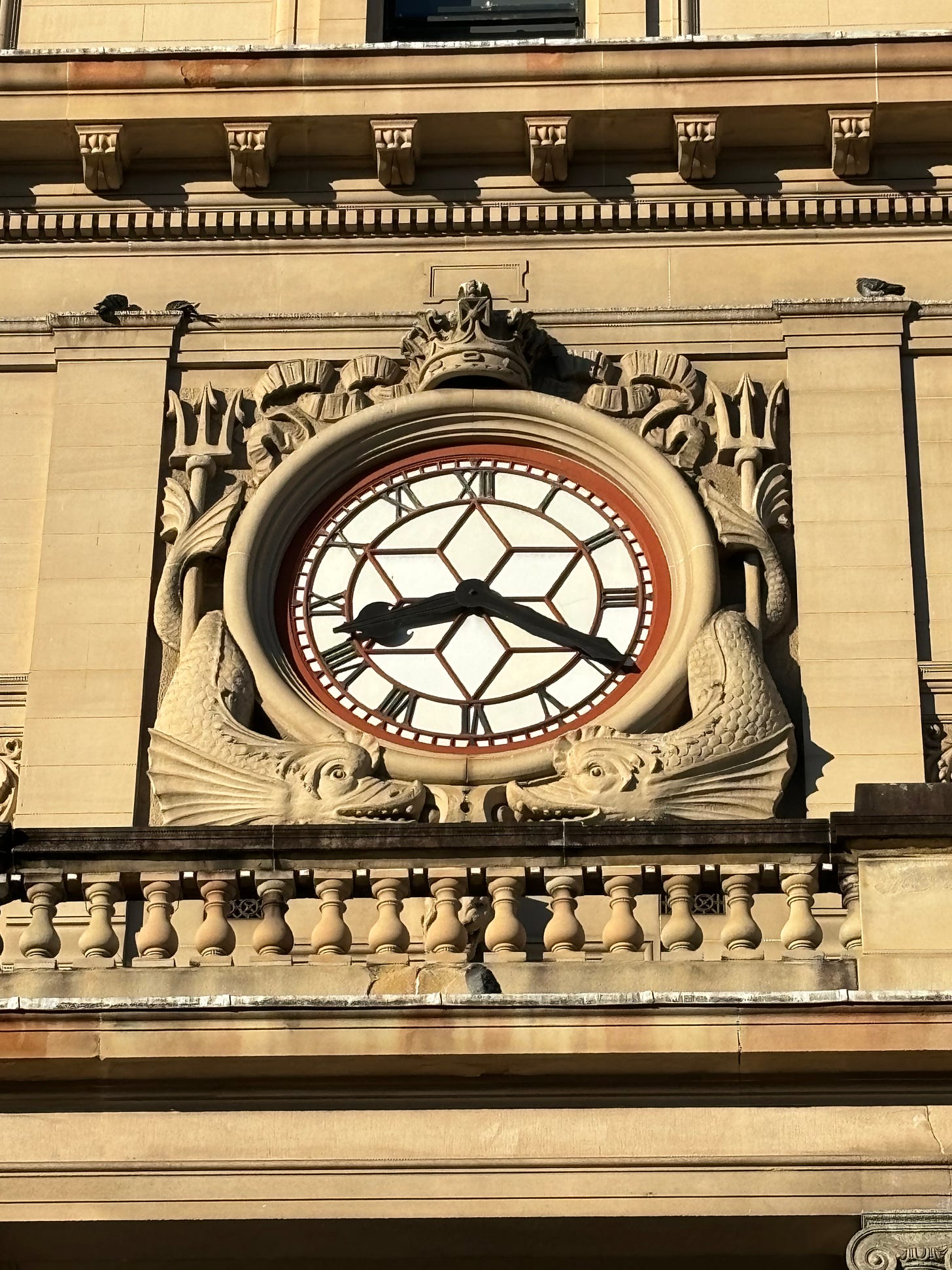 Heraldic dolphins and tridents on either side of a large ornamental clock on the facade of the Customs House in Sydney, Australia