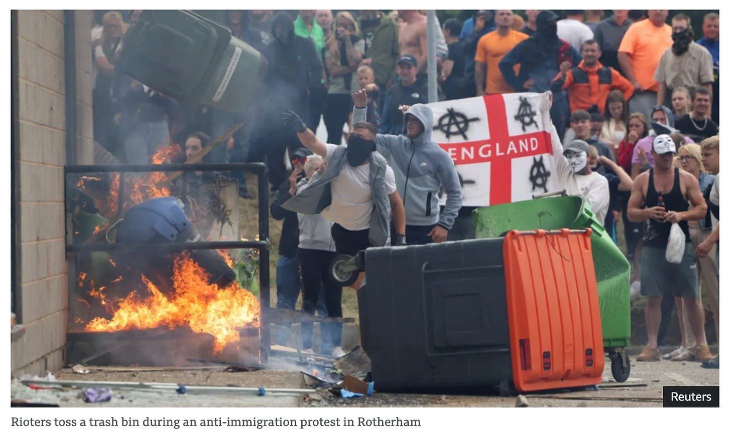 Rioters tossing a trash bin into a fire.