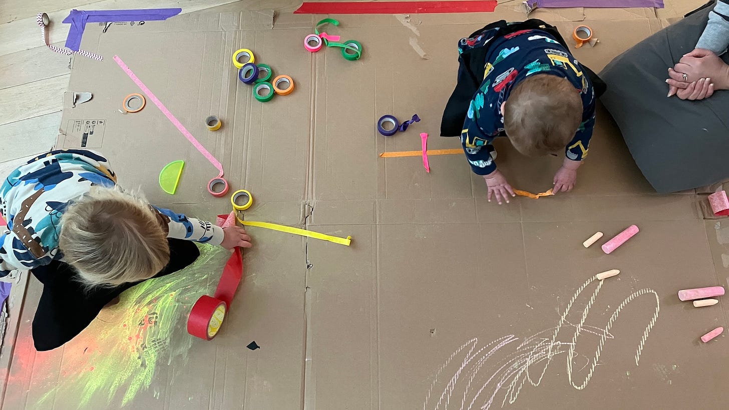 children sitting on cardboard with brightly coloured tape and chalk