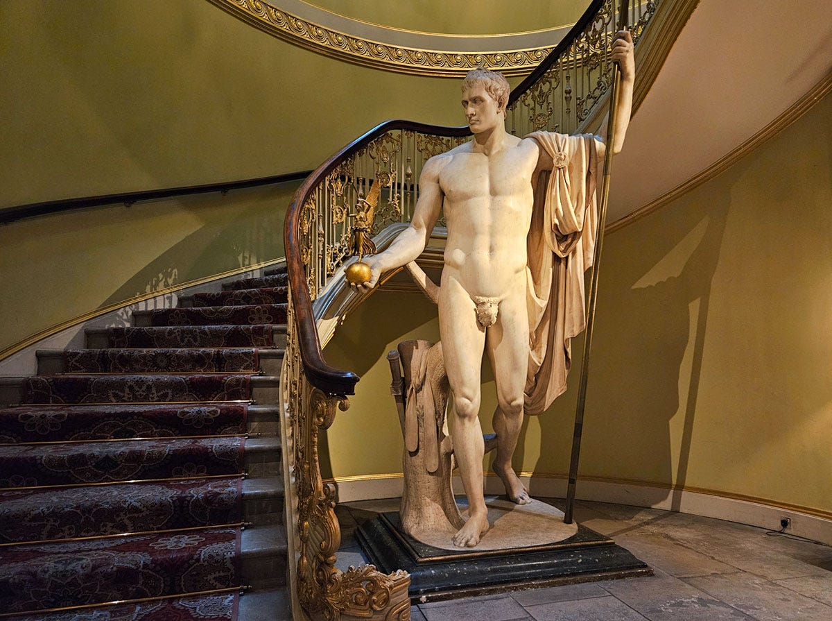 A large statue of a naked man in front of a large staircase