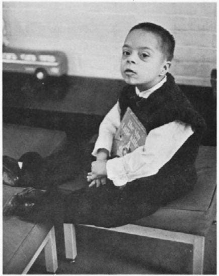 A boy sits holding a children's book, "The Shy Little Kitten."