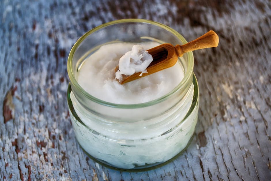 Close-up of organic coconut oil in glass jar with wooden spoon, perfect for natural health and wellness use.