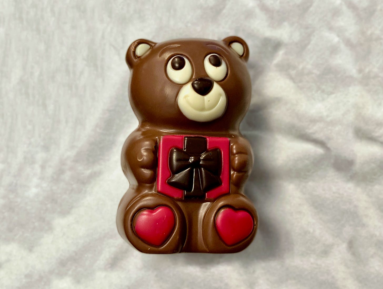 Chocolate bear holding a gift with love hearts on its feet
