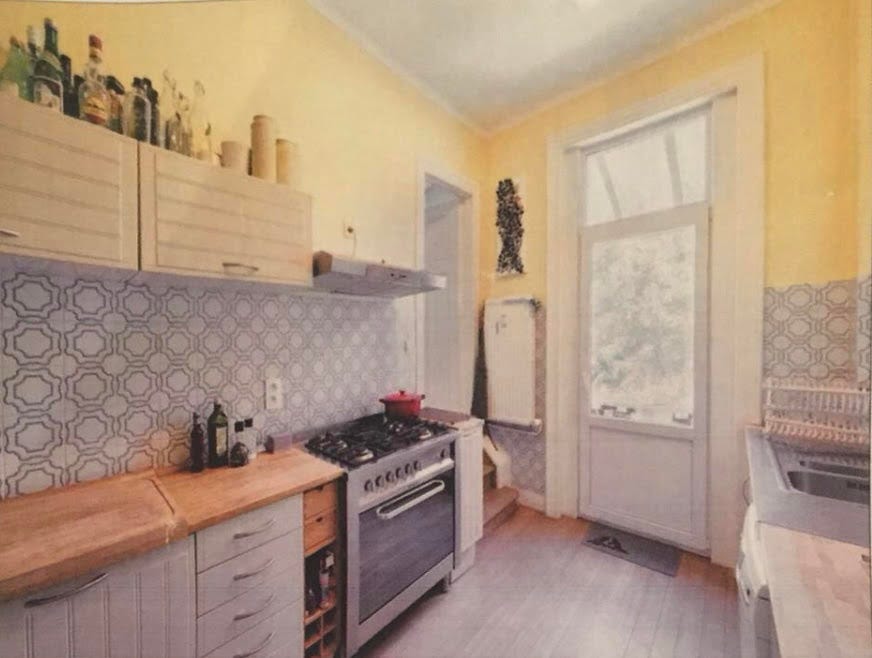 Old Kitchen with stove and cupboards on one side, sink on the other and window in the middle.