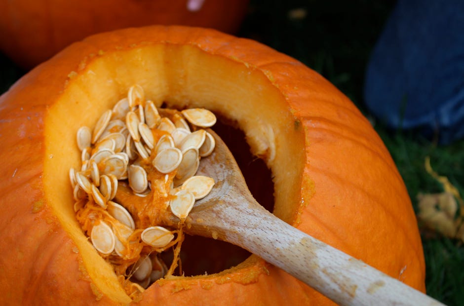 a pumpkin with the top cut off and a wooden spoon scooping out the seeds and stringy goop