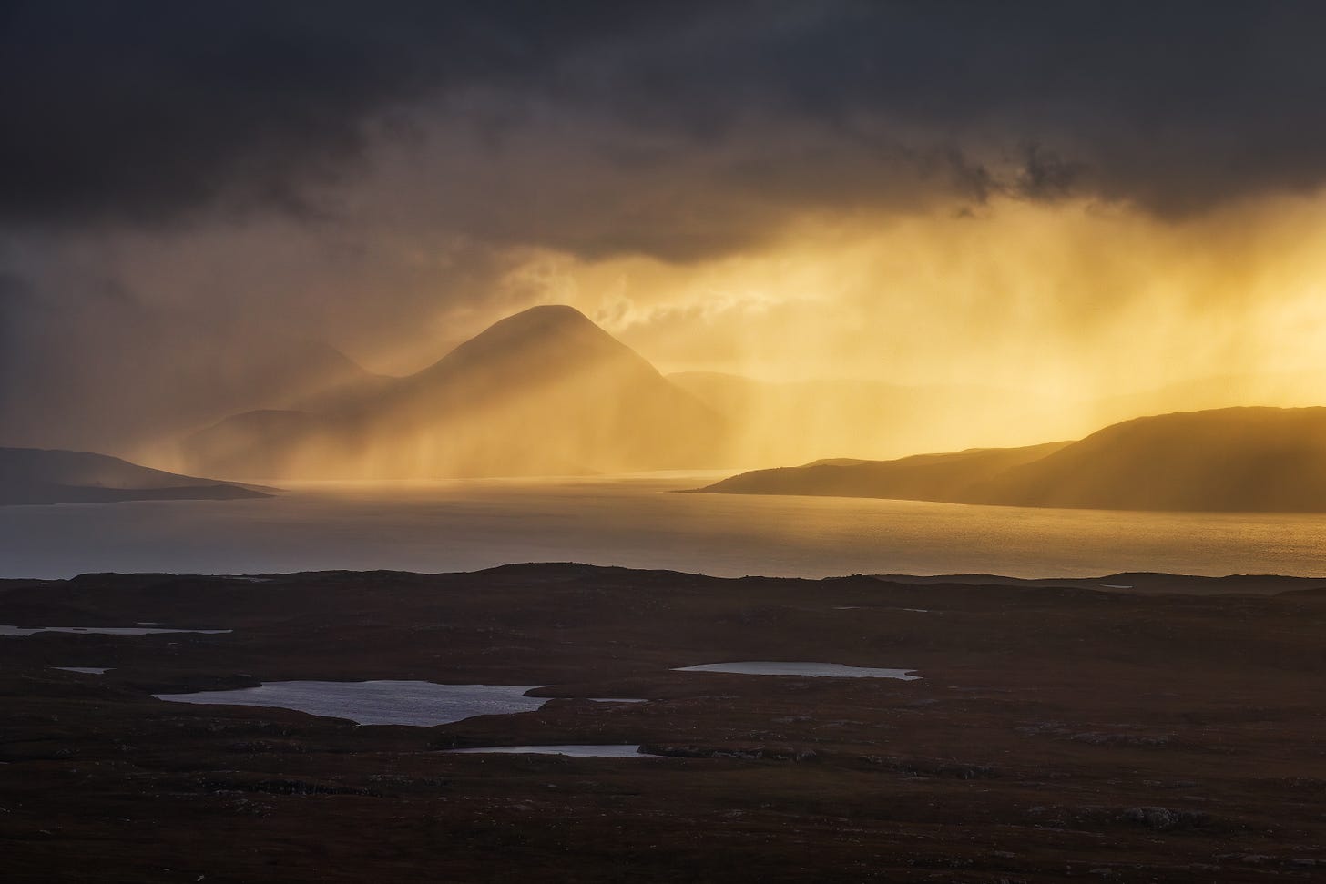 Rain is illuminated by the setting sun revealing the silhouettes of distant mountains