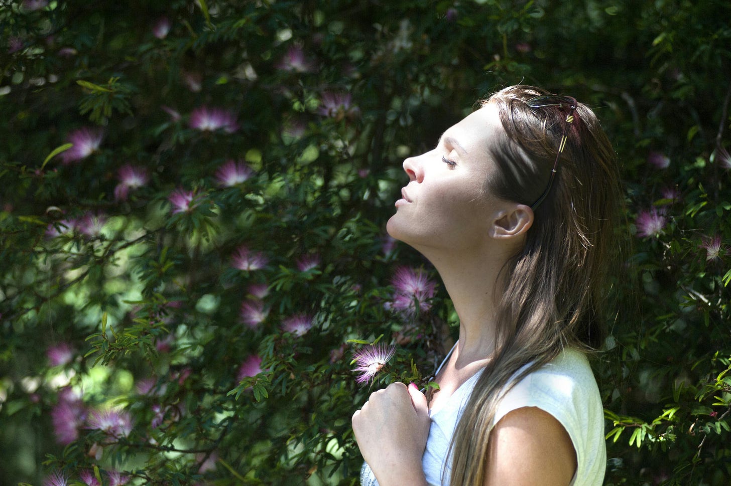 Photo of woman amid flowering trees with eyes closed and lips relaxed