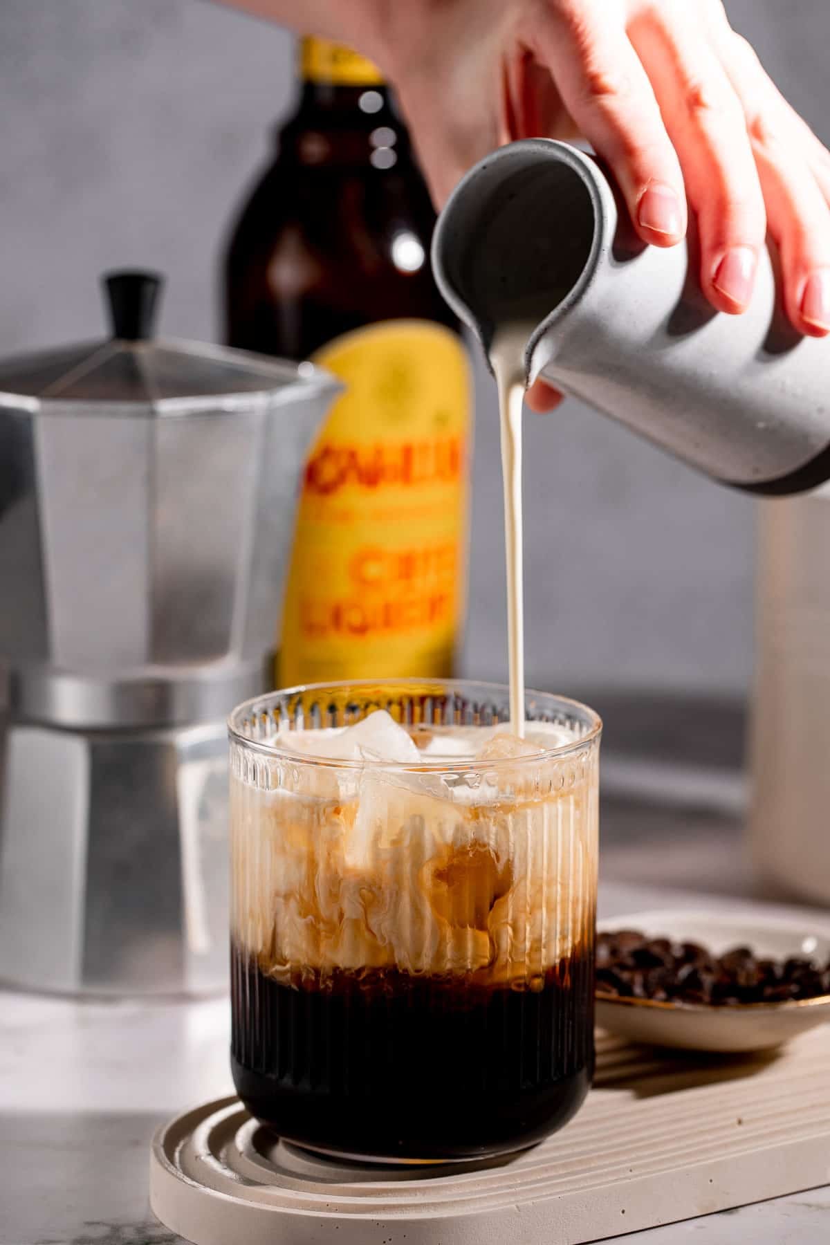 Cream pouring into a coffee cocktail filled with ice.