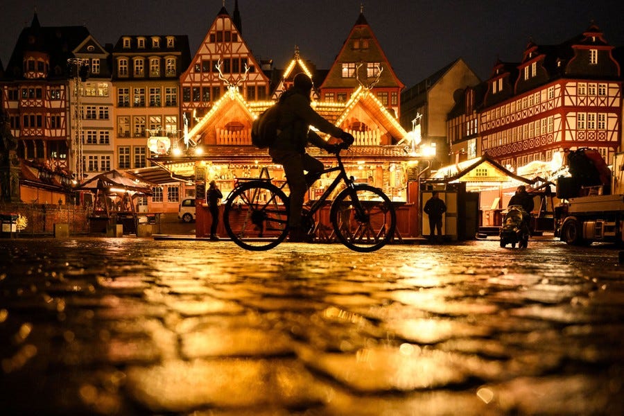 A person rides a bicycle past a Christmas marketplace.